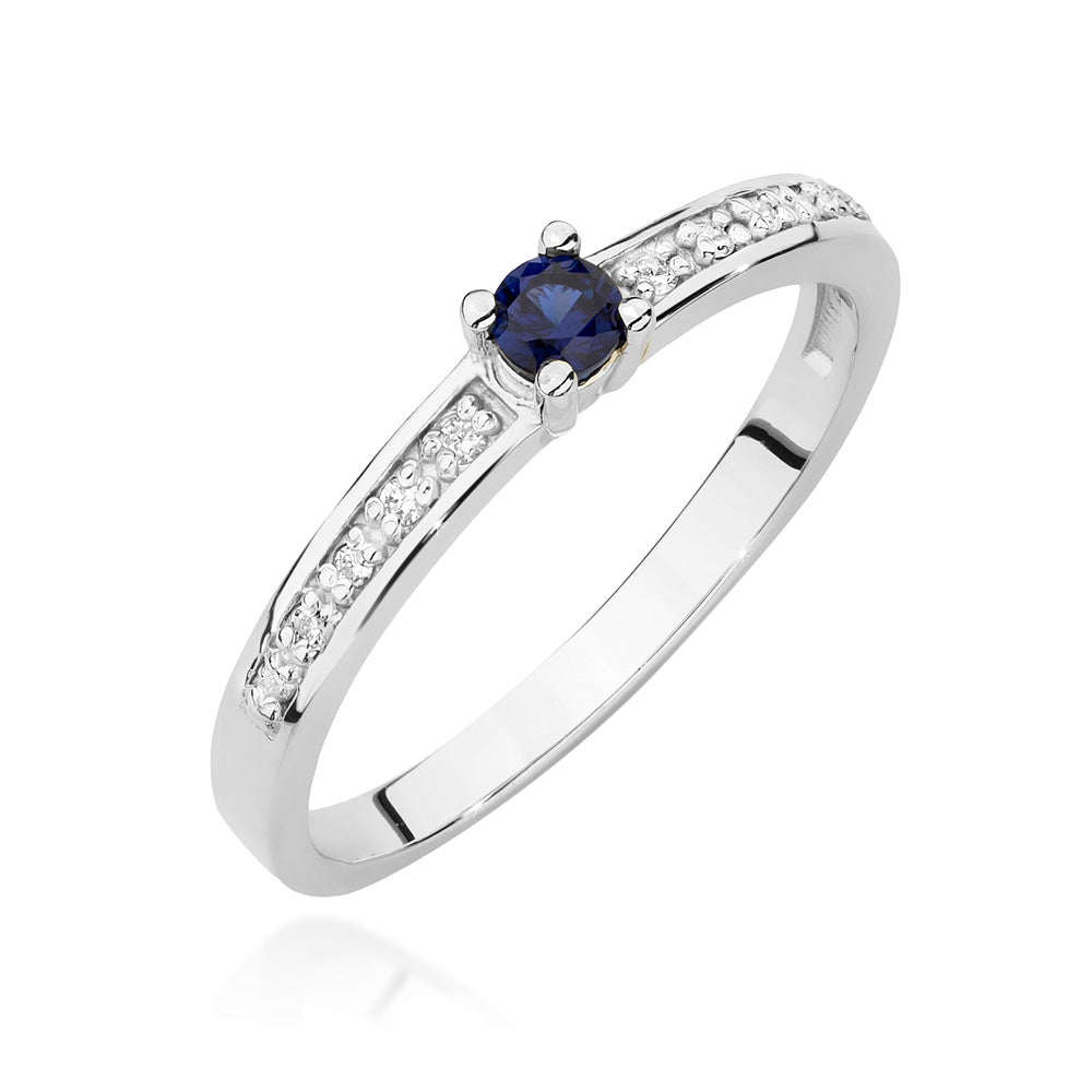 Ein weißgoldener Verlobungsring mit einem zentralen Saphir und seitlich eingefassten Diamanten. Der Ring zeigt ein modernes und elegantes Design mit klaren Linien und funkelnden Akzenten.