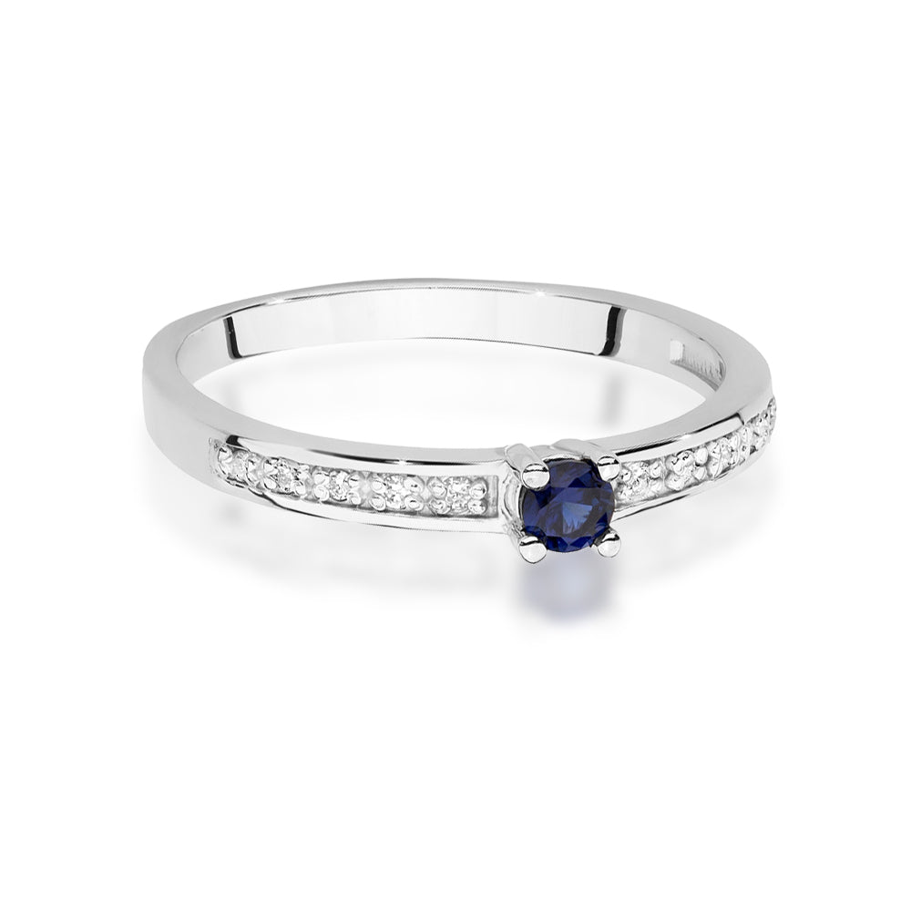 Ein detailliertes Bild eines Verlobungsrings aus Weißgold mit einem zentralen blauen Saphir und kleineren Diamanten entlang der Ringschiene. Die sorgfältige Verarbeitung und das glänzende Finish sind gut erkennbar.
