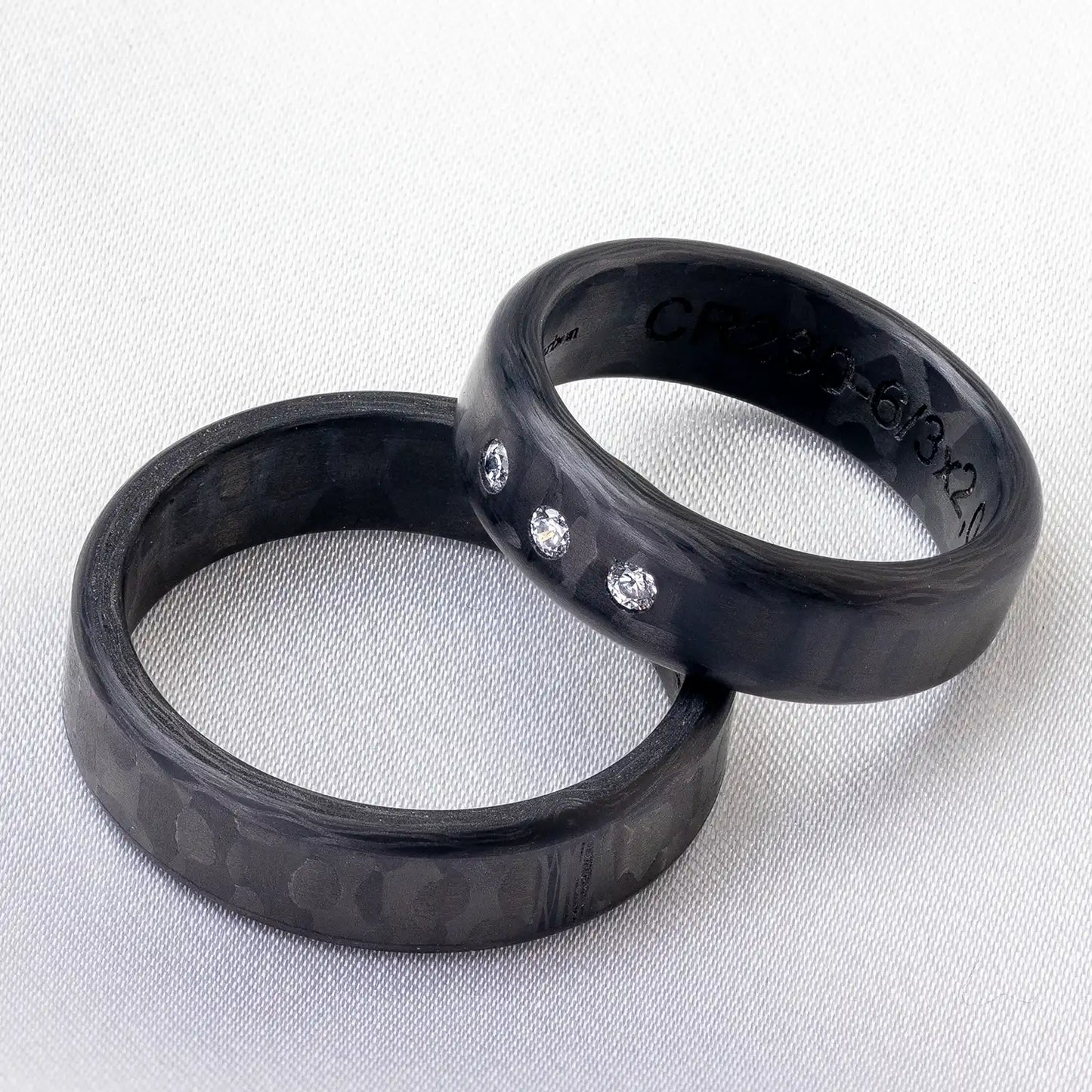 Schwarze Carbon Trauringe auf einem hellen Hintergrund, einer mit drei Diamanten.