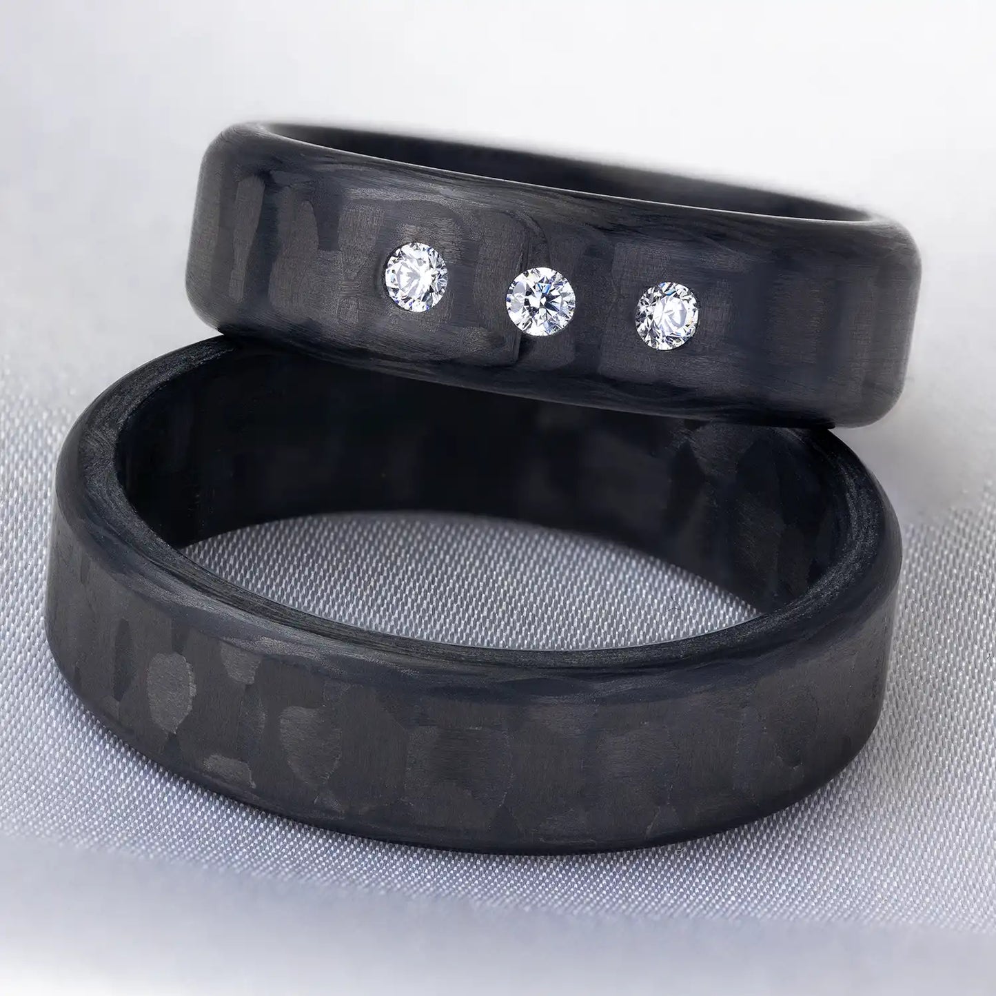 Nahaufnahme von zwei schwarzen Carbon Eheringen, der eine mit drei Diamanten verziert.