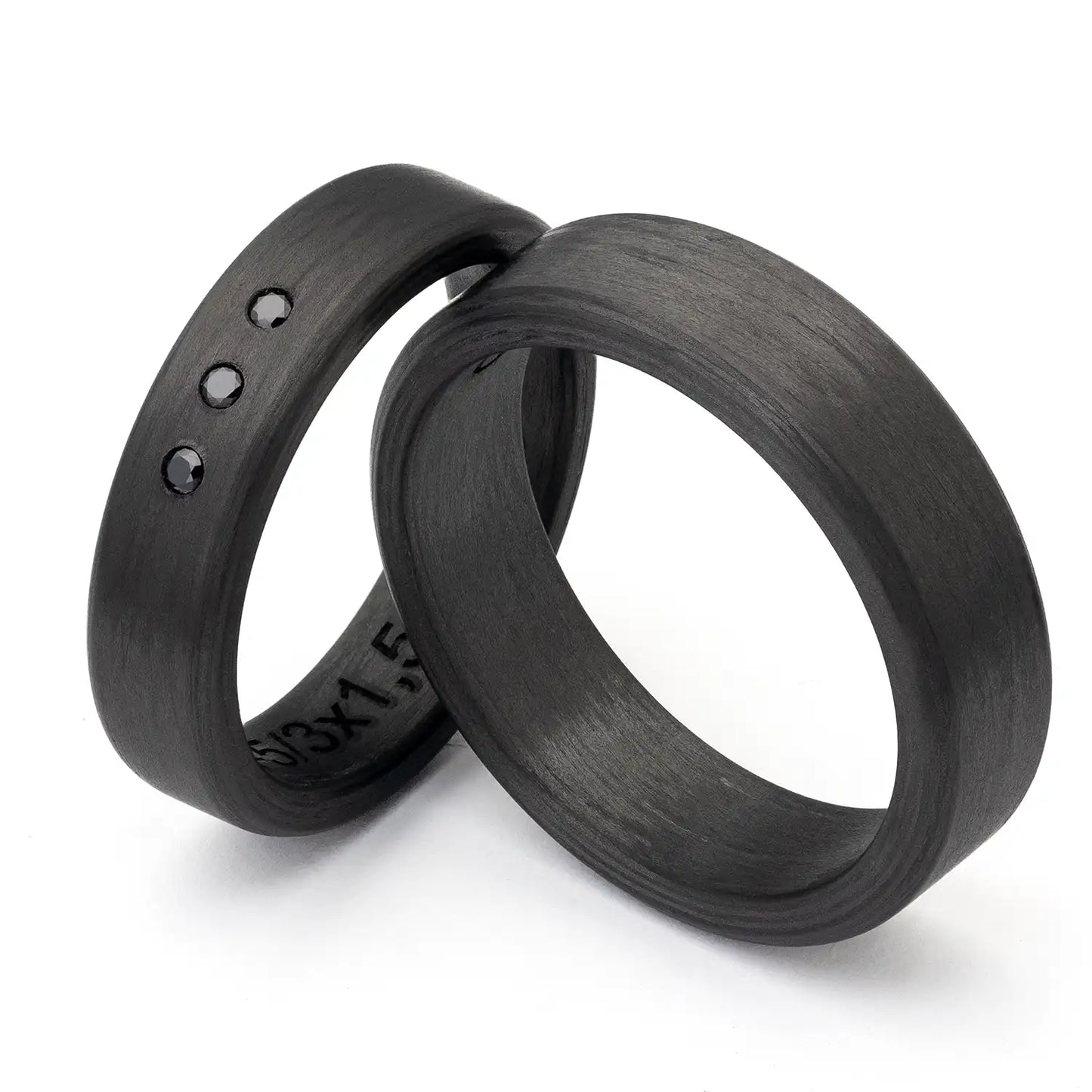 Zwei schwarze Carbon Eheringe auf weißem Hintergrund, einer mit drei schwarzen Zirkonia.