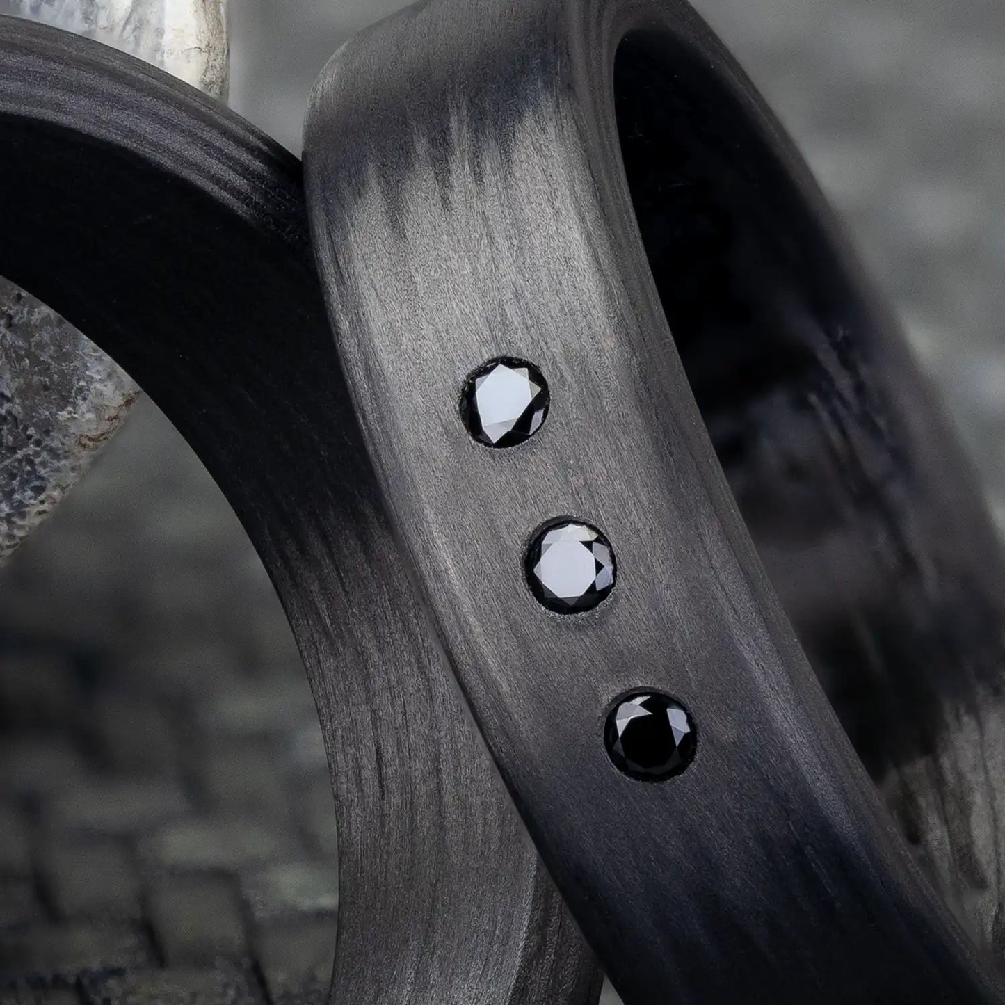 Nahaufnahme von zwei Carbon Trauringen, einer mit drei schwarzen Zirkonia.