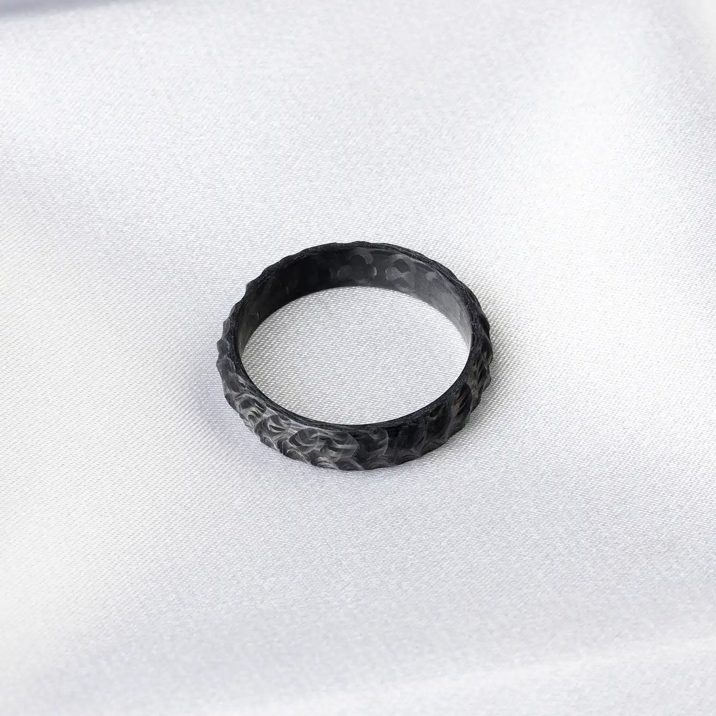 Schwarzer Carbonring mit unregelmäßiger Struktur auf einem weißen, strukturierten Hintergrund