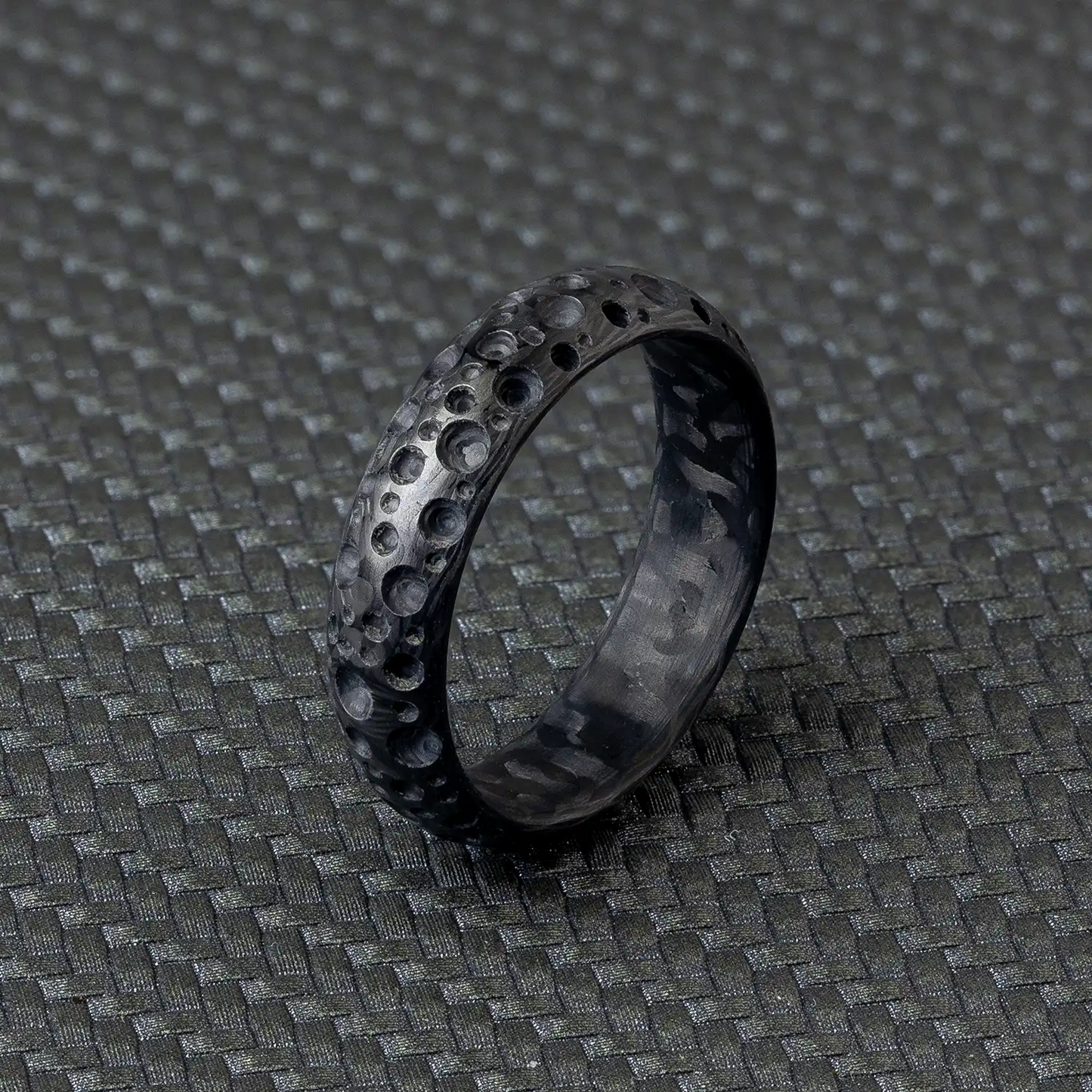 Ein schwarzer Carbonfaser-Ring mit einer Breite von 6 mm und einer Höhe von 2,2 mm, auf einer strukturierten Oberfläche platziert.