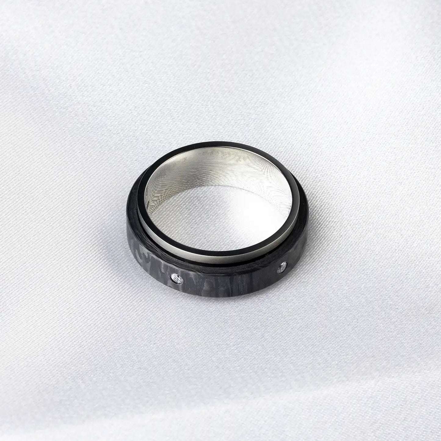 Schwarzer Ring aus Kohlefaser und Titan mit Diamanten, auf weißem Stoffhintergrund.