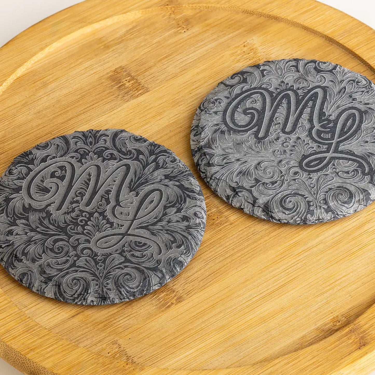 Detailaufnahme von runden Schieferuntersetzern mit personalisiertem Monogramm und kunstvollen Gravuren – edles Design für anspruchsvolle Einrichtung.