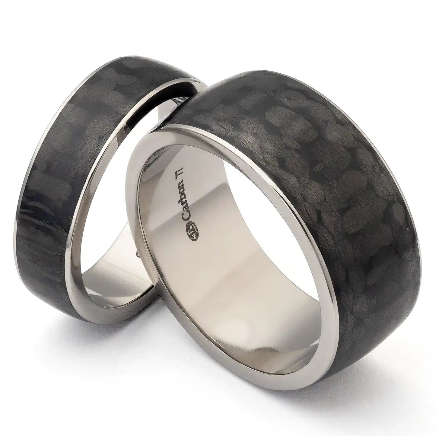 Zwei schwarze Eheringe aus Titan und Karbonfaser auf weißem Hintergrund, mit einer Gravur im Inneren des Rings.