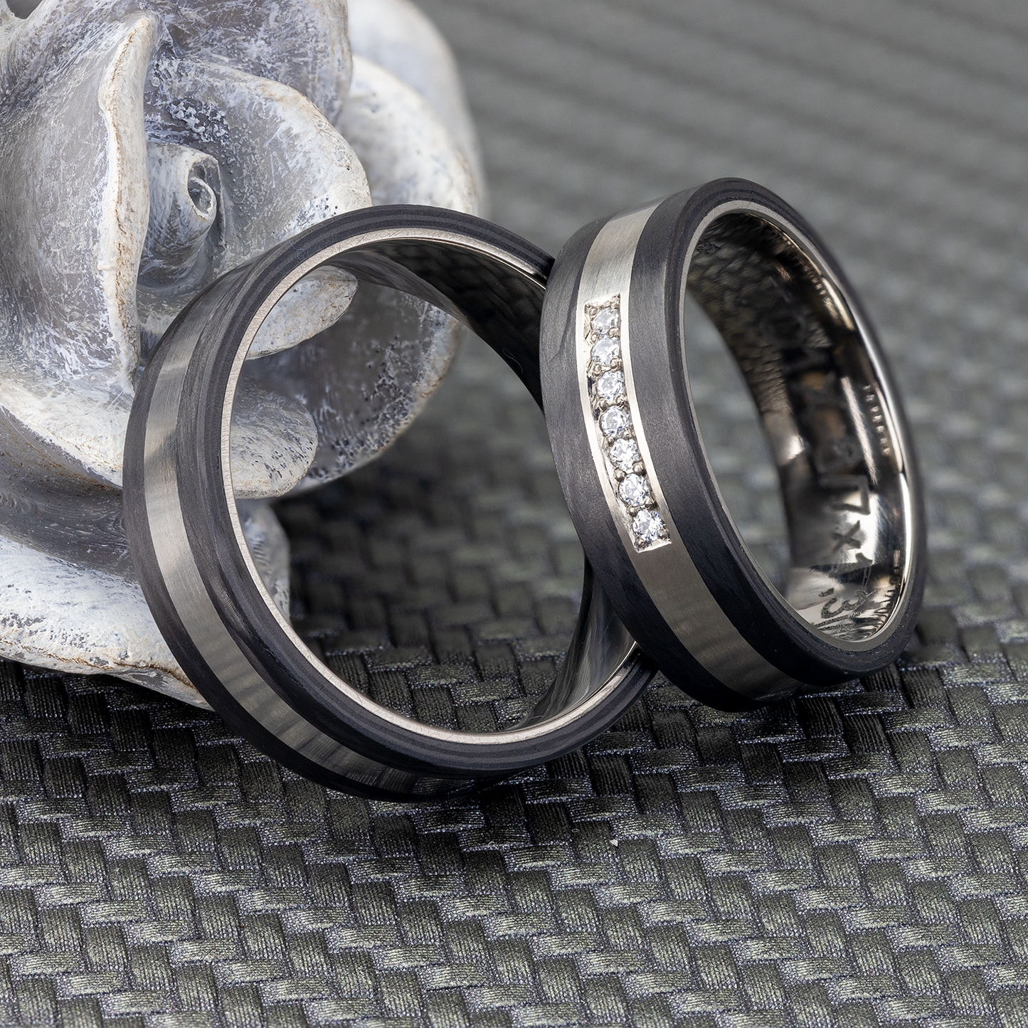 Titan- und Carbon-Eheringe mit 7 Zirkonia, präsentiert vor einer grauen Rose.