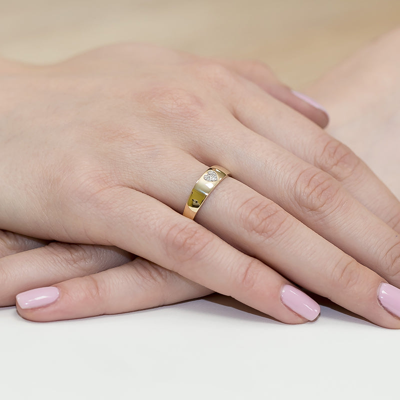 Dieses Bild zeigt zwei Hände, von denen eine einen goldenen Ring mit einem herzförmigen Diamanten trägt. Die Hände sind übereinander gelegt, und die Nägel sind in einem zarten Rosa lackiert.