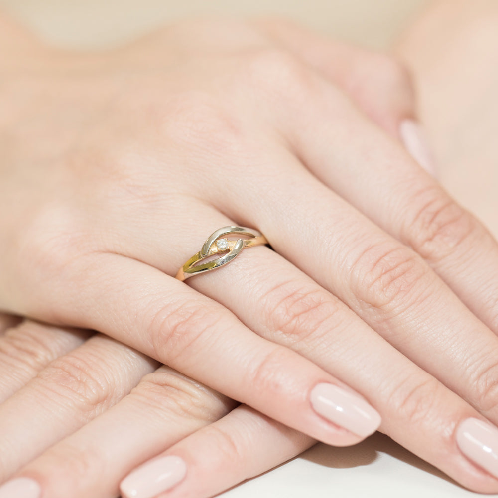 Eleganter Verlobungsring aus 14K Gelbgold mit einem funkelnden Diamanten auf einer Hand getragen. Der Ring hat ein stilvolles, ineinander greifendes Design.