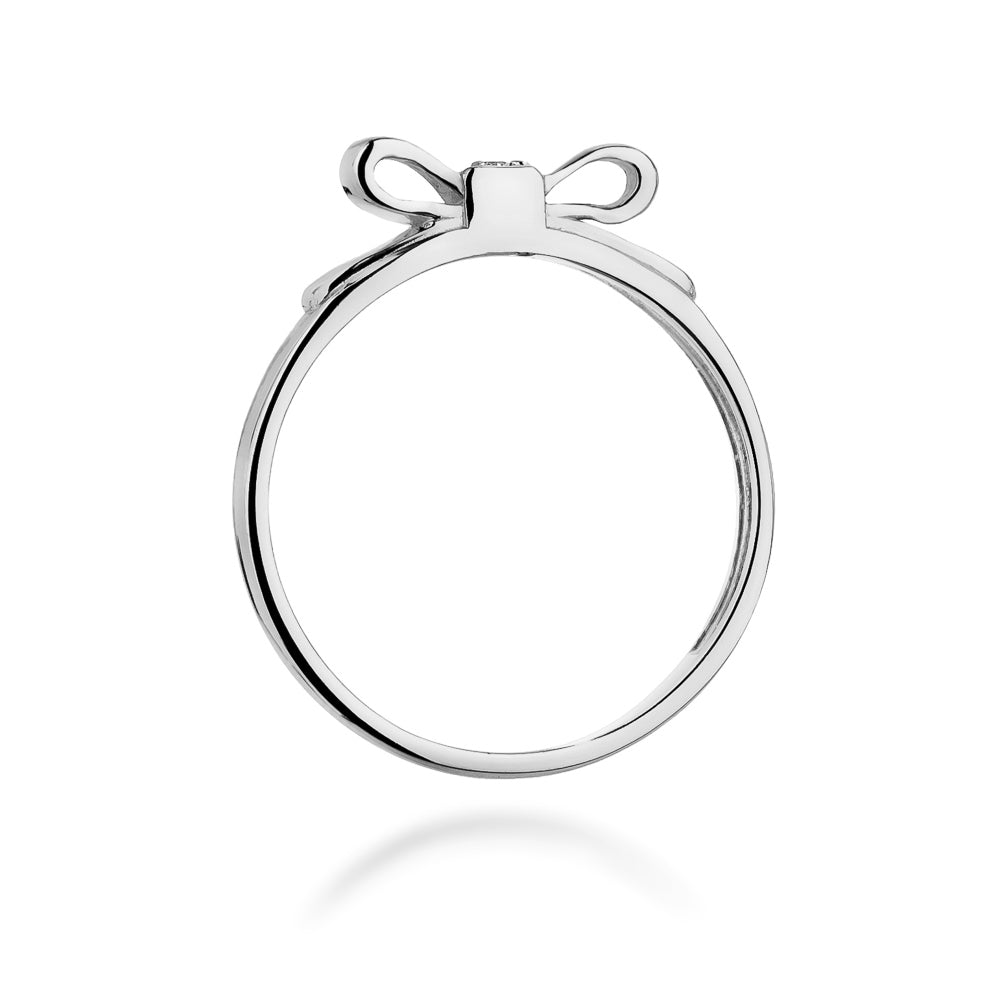 Ein seitlicher Blick auf einen Silberring mit einer Schleife und einem kleinen Diamanten. Der Ring hat ein elegantes und glänzendes Finish.