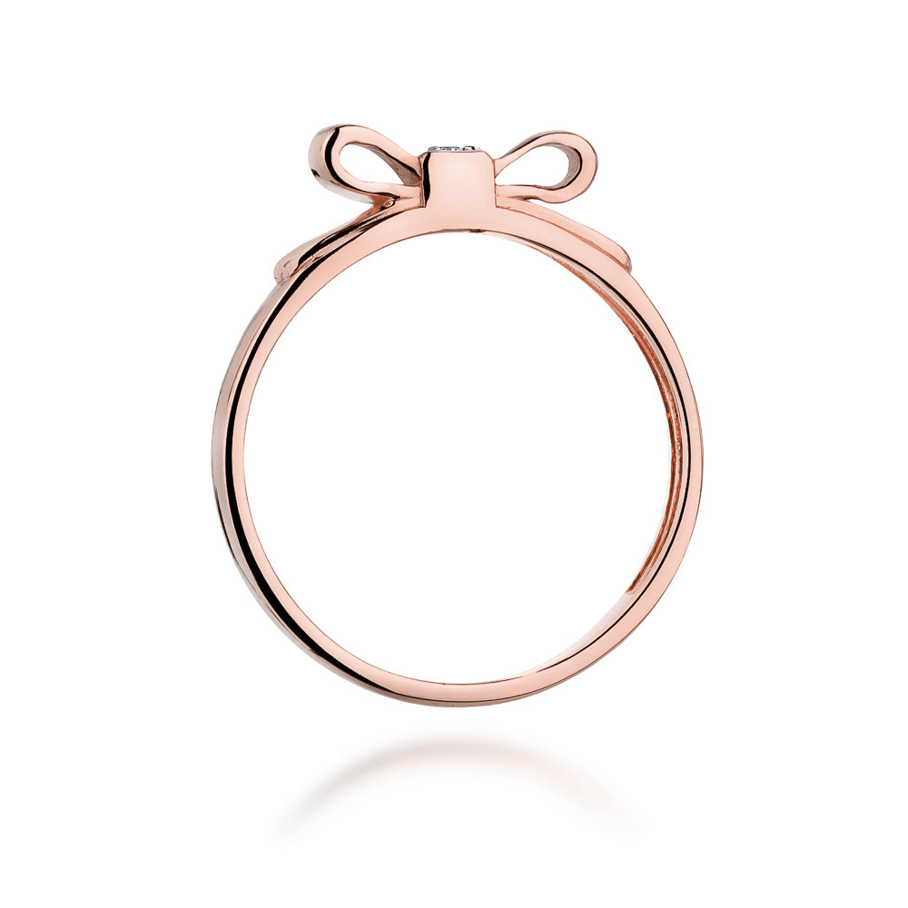 Ein seitlicher Blick auf einen Roségold-Ring mit einer Schleife und einem kleinen Diamanten. Der Ring hat ein elegantes und glänzendes Design.