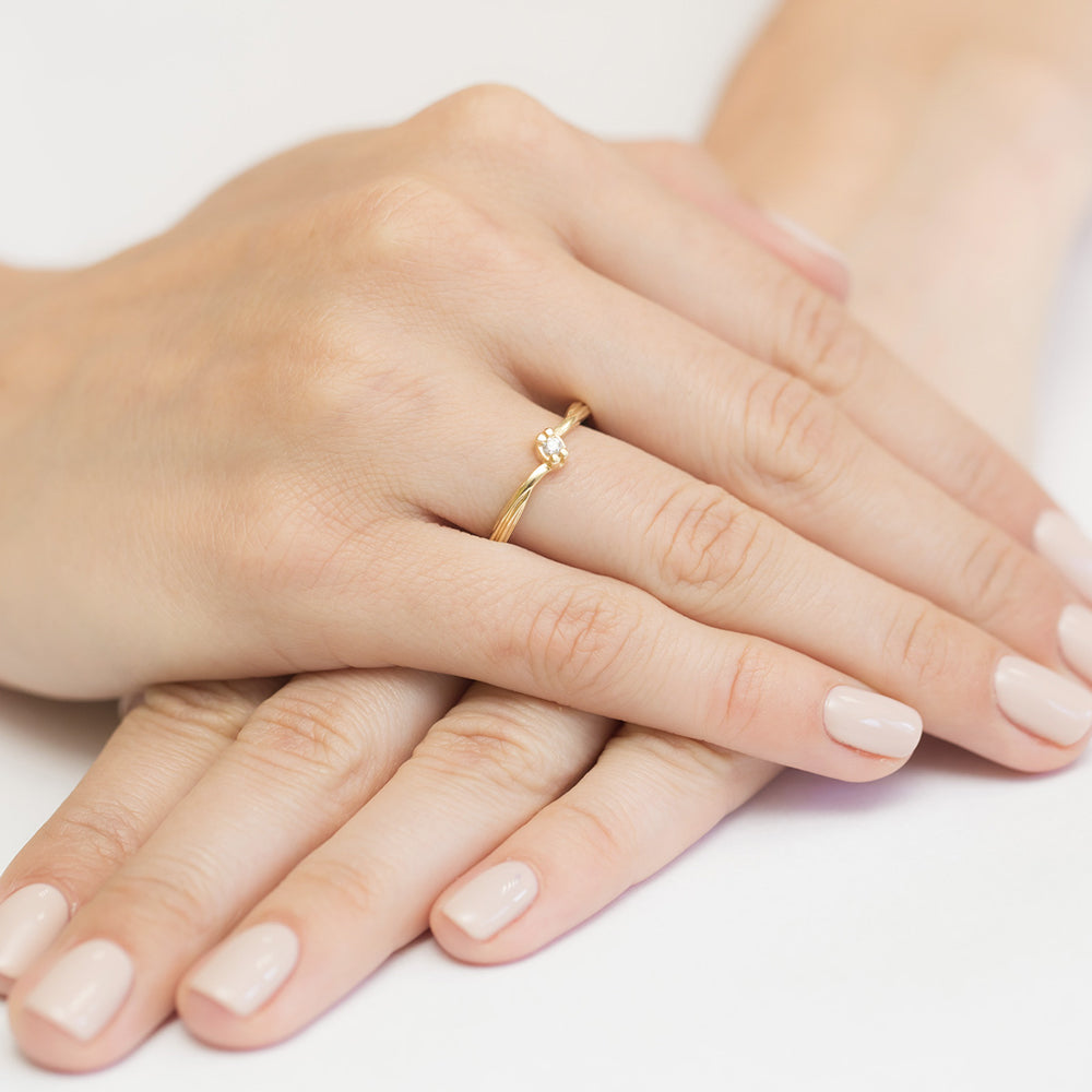 Nahaufnahme einer Hand mit einem eleganten Verlobungsring aus Gelbgold, der mit einem einzelnen funkelnden Diamanten besetzt ist.