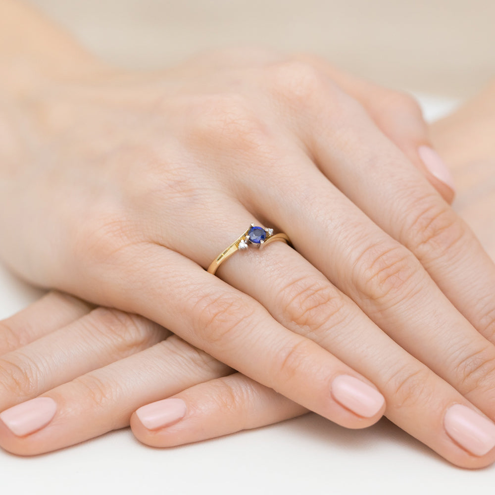 Eleganter Verlobungsring aus Gold 585 mit einem runden blauen Saphir in der Mitte und zwei funkelnden Diamanten an den Seiten, getragen an einer Hand.