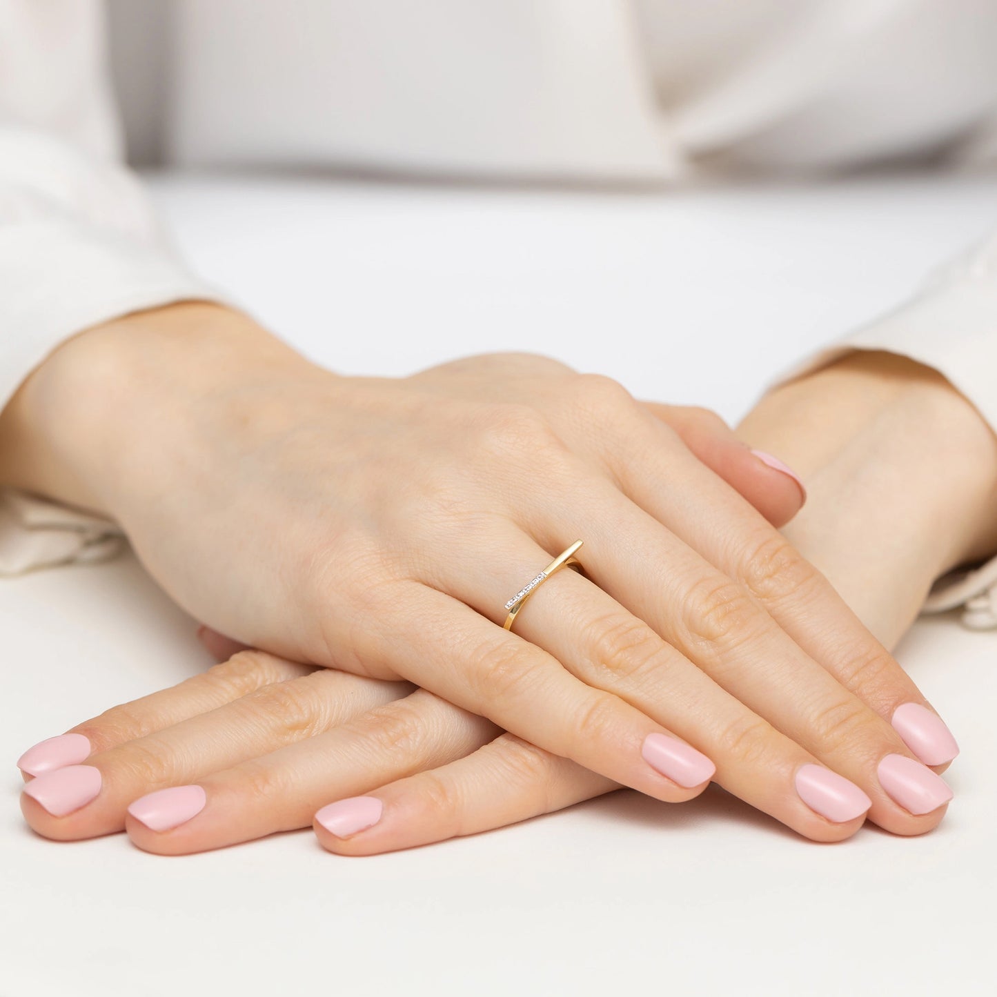 Diese Nahaufnahme zeigt die zarten Hände einer Person, die einen eleganten, schmalen Ring aus Gelbgold trägt. Der Ring ist modern und schlicht gestaltet, mit einer dünnen Stange, die sich über den Finger erstreckt. Die Nägel der Person sind in einem weichen Rosa lackiert, was die Eleganz des Rings unterstreicht.