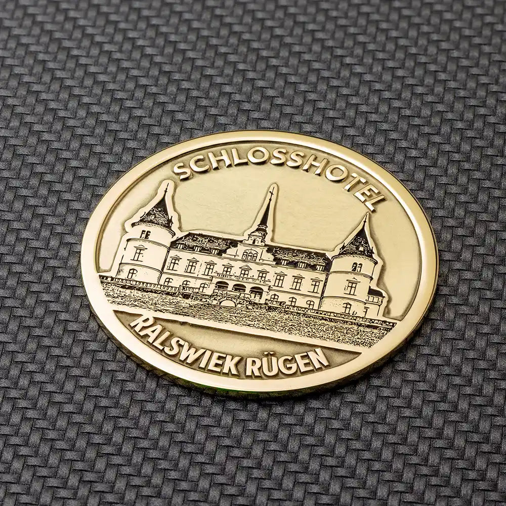 Runde goldene Münze mit der Gravur des Schlosshotels Ralswiek und der Inschrift "SCHLOSSHOTEL RALSWIEK RÜGEN". münze selbst gestalten.