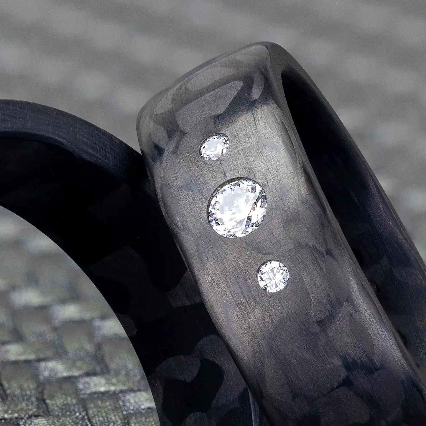 Nahaufnahme eines schwarzen Carbon Eherings mit 3 Diamanten, gezeigt auf einem gewebten Hintergrund.