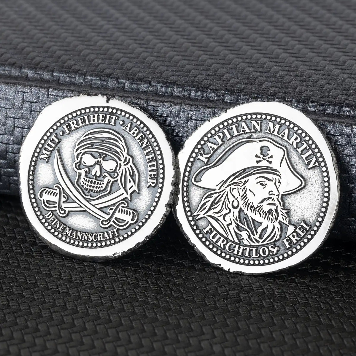 Beide Seiten der personalisierten Piratenmünze aus 925er Silber mit Kapitänsporträt und Totenkopf über gekreuzten Säbeln