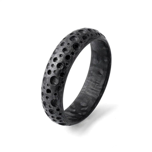 Nahaufnahme eines schwarzen Carbonfaser-Rings mit mondkraterähnlicher Textur auf weißem Hintergrund.