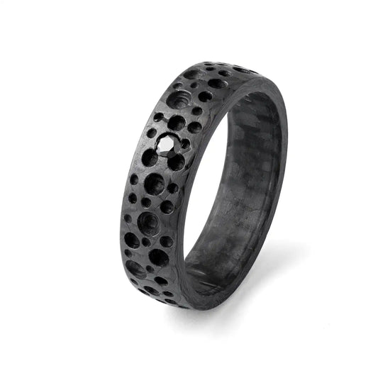 Nahaufnahme eines schwarzen Carbonrings mit Mondkratertextur und einem schwarzen Diamanten oder Zirkonia auf weißem Hintergrund.