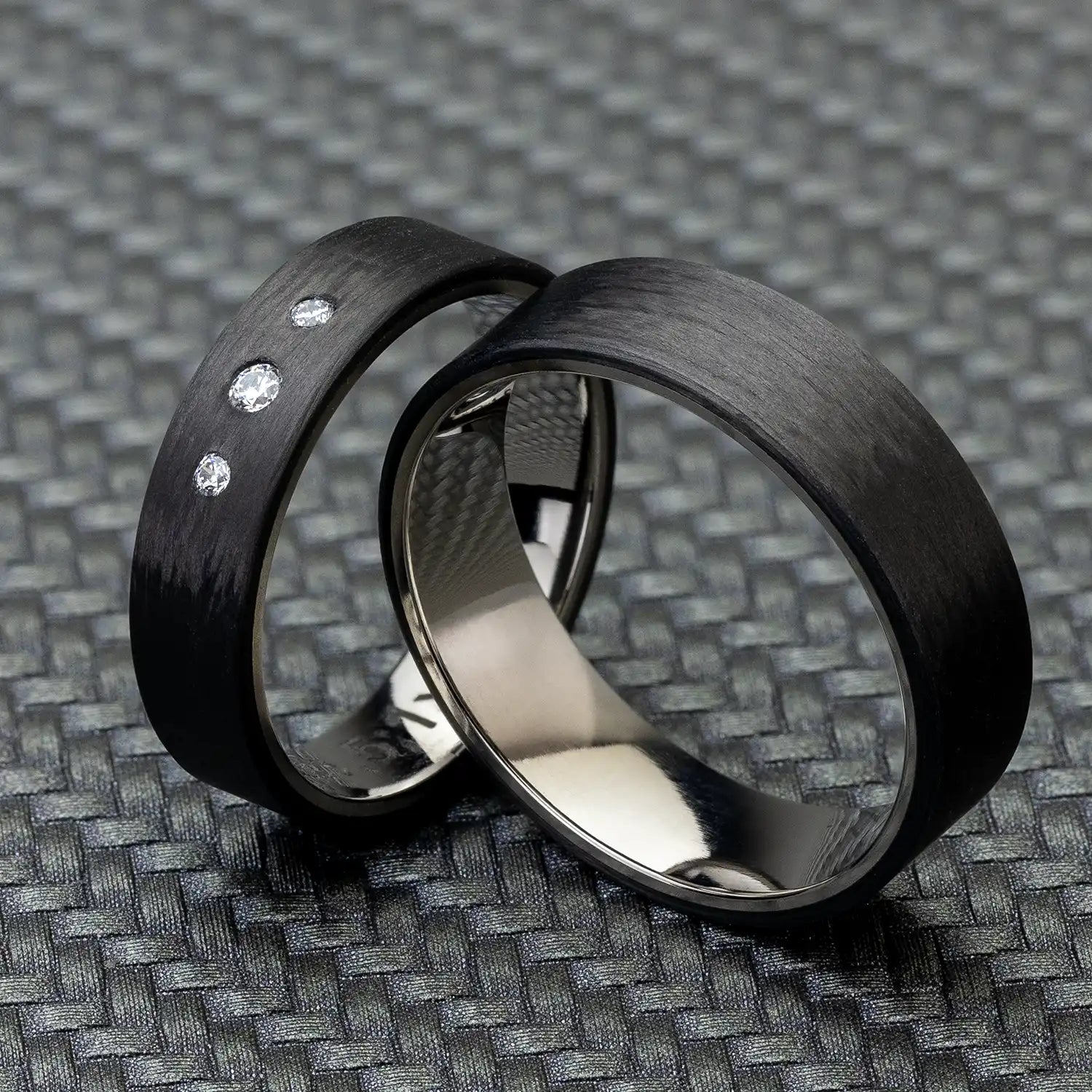 Zwei schwarze Carbon und Titan Eheringe mit Zirkonia, auf strukturiertem Hintergrund fotografiert.