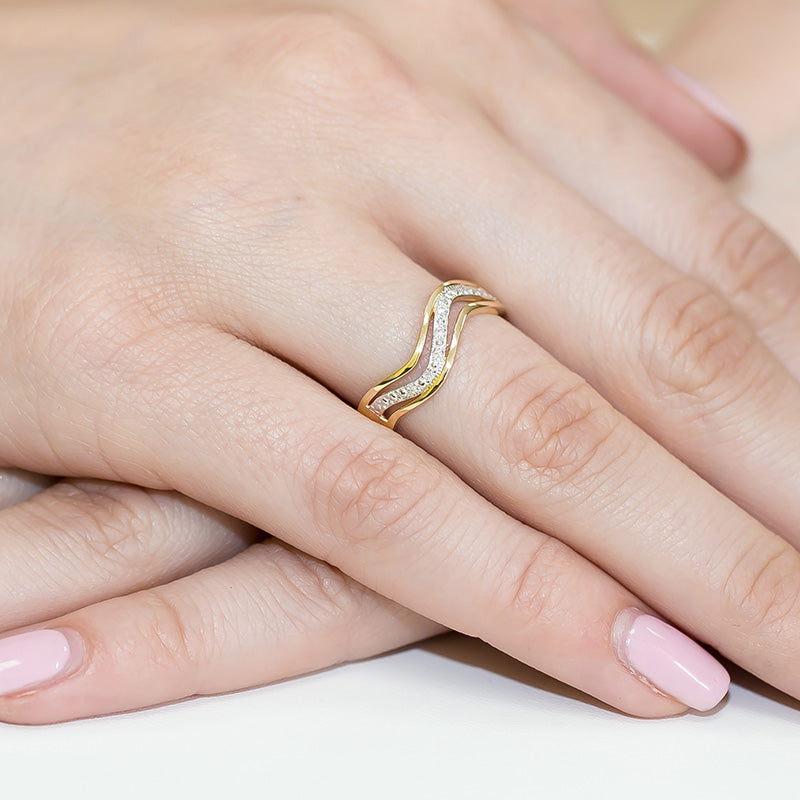 Nahaufnahme einer Hand mit einem eleganten Verlobungsring aus Gold 585. Der Ring hat ein einzigartiges Wellen-Design und ist mit Diamanten besetzt. Die Hand hat gepflegte, rosa lackierte Fingernägel.