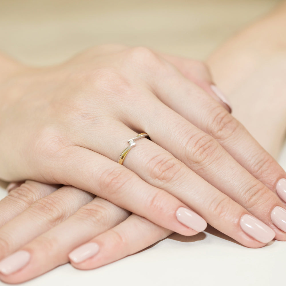 Elegante Hände mit einem goldenen Verlobungsring, der einen kleinen Diamanten in der Mitte hält.