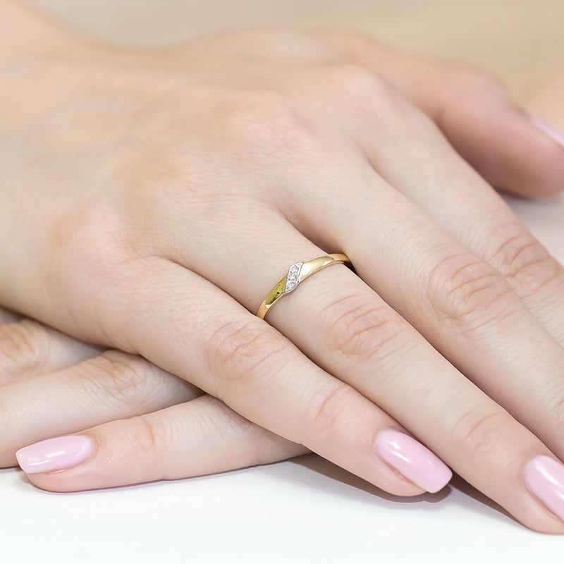 Der zierliche Verlobungsring ist auf einer Hand abgebildet. Er besteht aus 14K Gold und ist mit Diamanten verziert. Die Fingernägel sind gepflegt und in einem zarten Rosa lackiert.