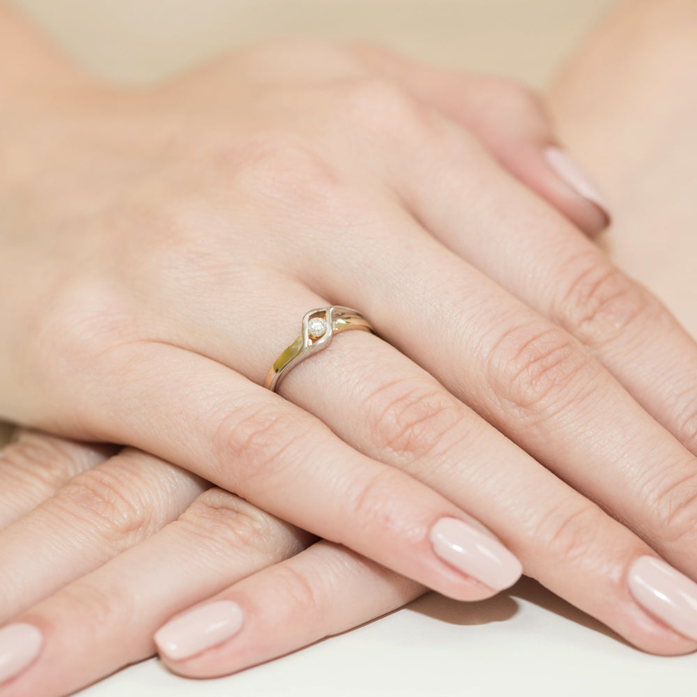 Nahaufnahme einer Hand mit einem eleganten Verlobungsring aus Gold 585 und einem Diamanten von 0,04 Karat. Der Ring hat ein elegantes und modernes Design mit einem zentralen Diamanten.