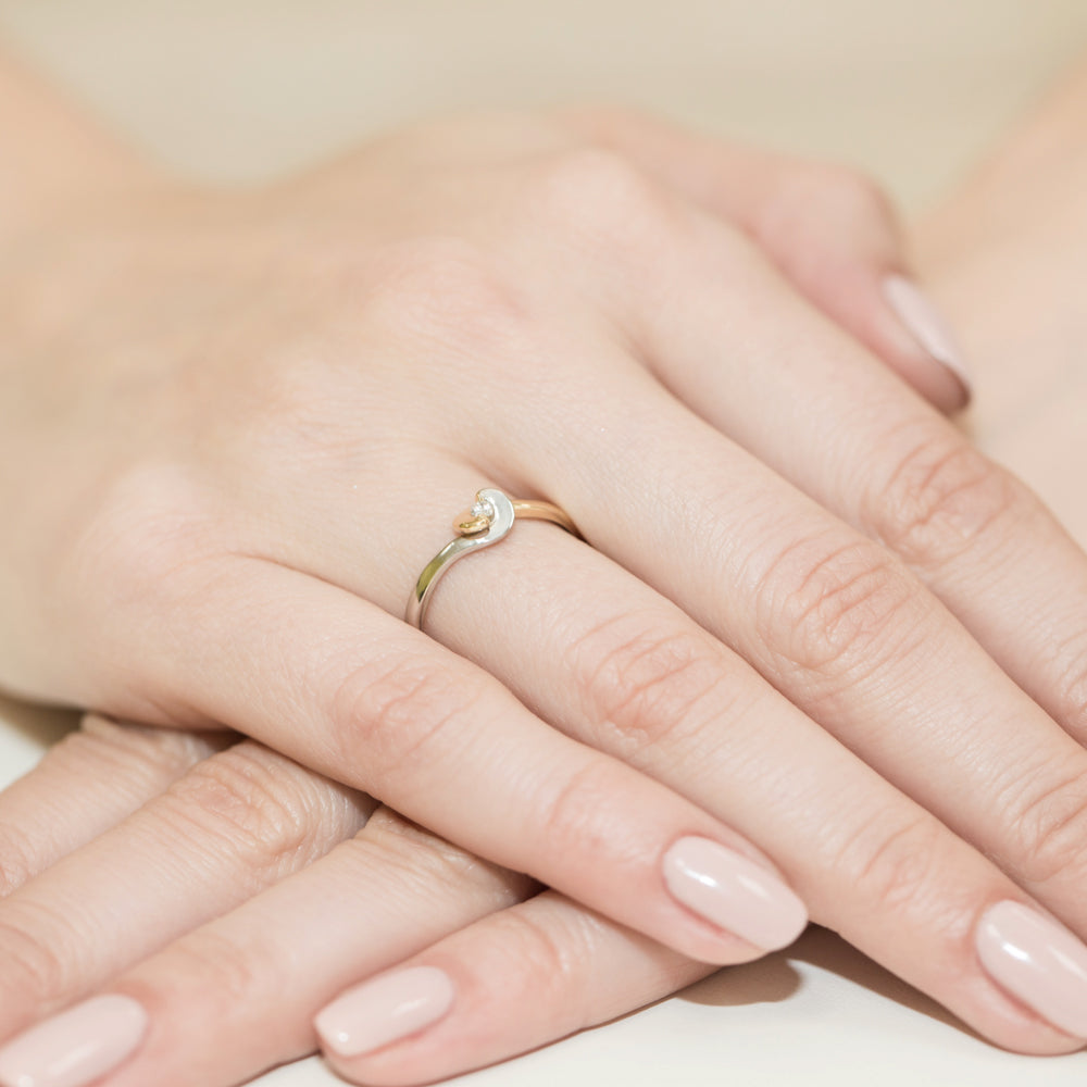 Nahaufnahme einer Hand mit einem eleganten Verlobungsring aus Gold 585 mit einem kleinen Diamanten. Die Fingernägel sind sauber manikürt und lackiert.