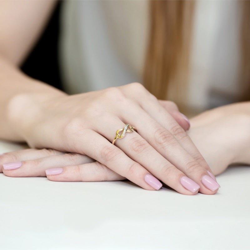 Nahaufnahme einer Hand, die einen eleganten goldenen Verlobungsring mit einem geschwungenen Design und mehreren Diamanten trägt. Die Nägel sind in einem zarten Rosa lackiert.