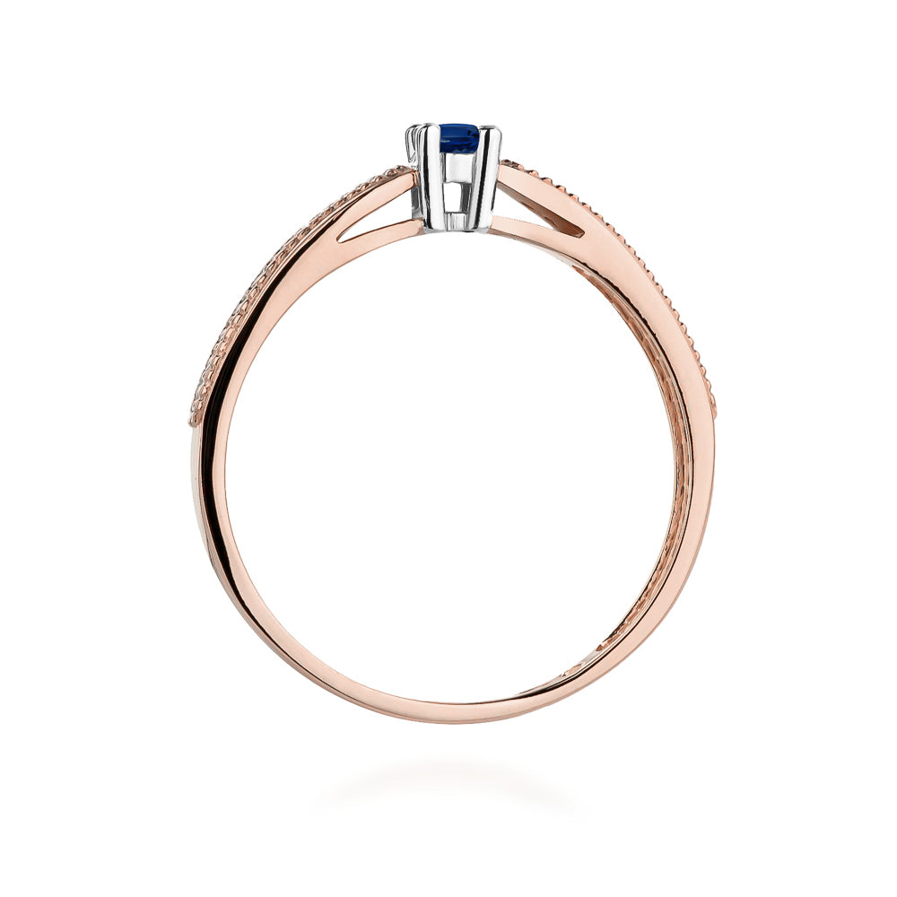 Der 14K Roségold Verlobungsring präsentiert sich mit einem strahlenden blauen Saphir in der Mitte, flankiert von funkelnden Diamanten. Ein zeitloses und edles Design.