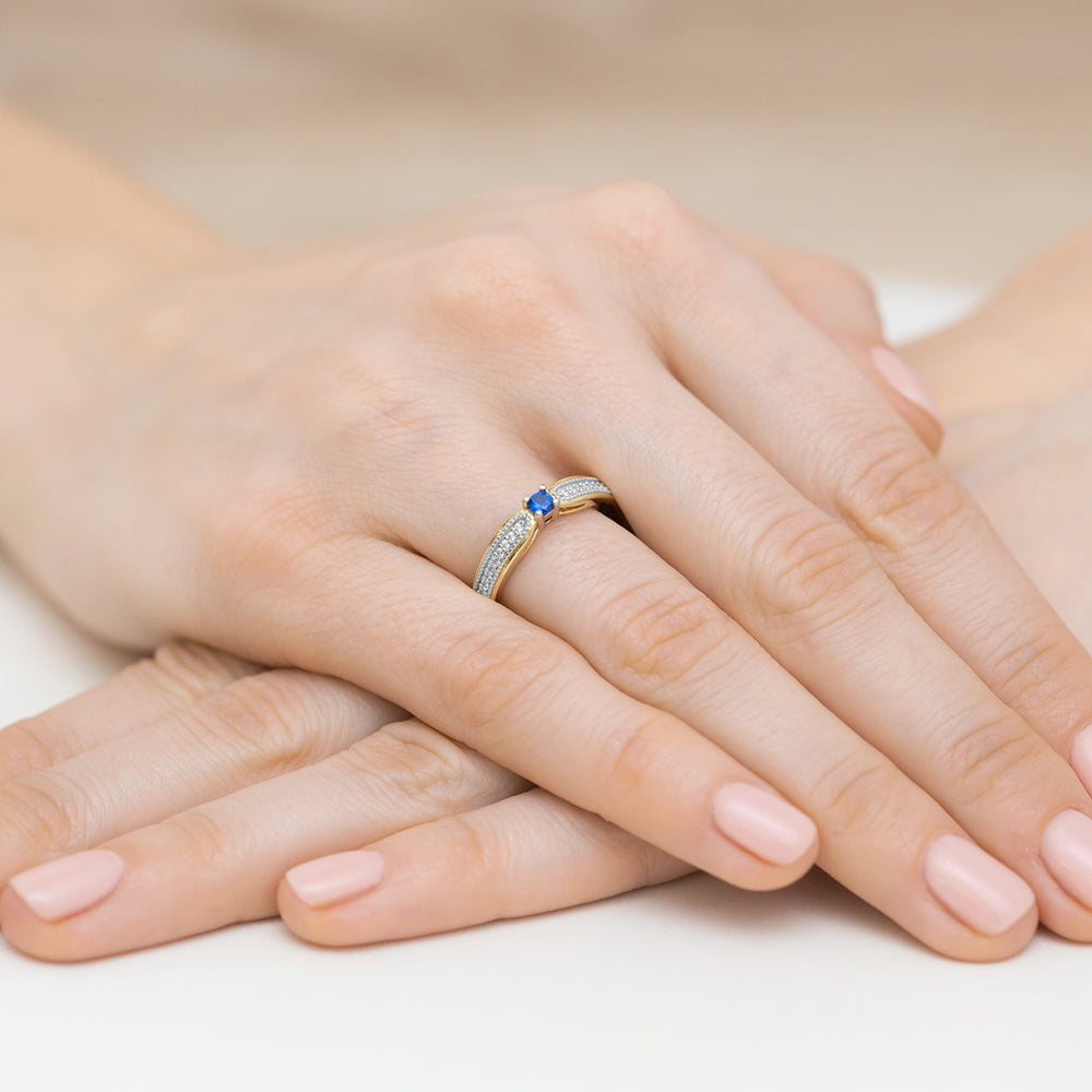 Dieser elegante Verlobungsring aus 14K Gold zeigt einen glänzenden blauen Saphir in der Mitte, umgeben von funkelnden Diamanten. Der Ring ist filigran gearbeitet und sitzt perfekt am Finger.